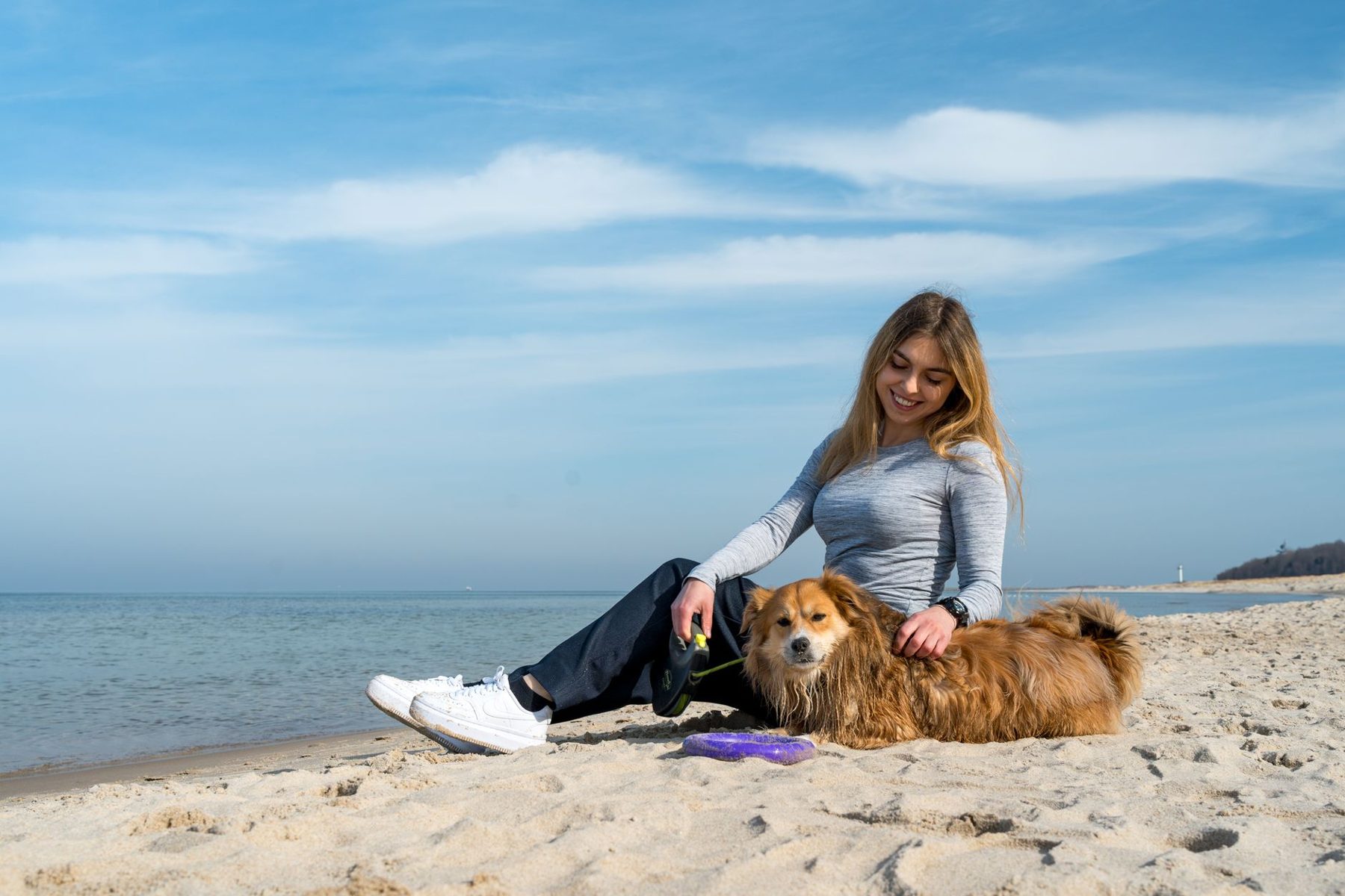 Smiling woman sitting on the beach with her fluffy dog